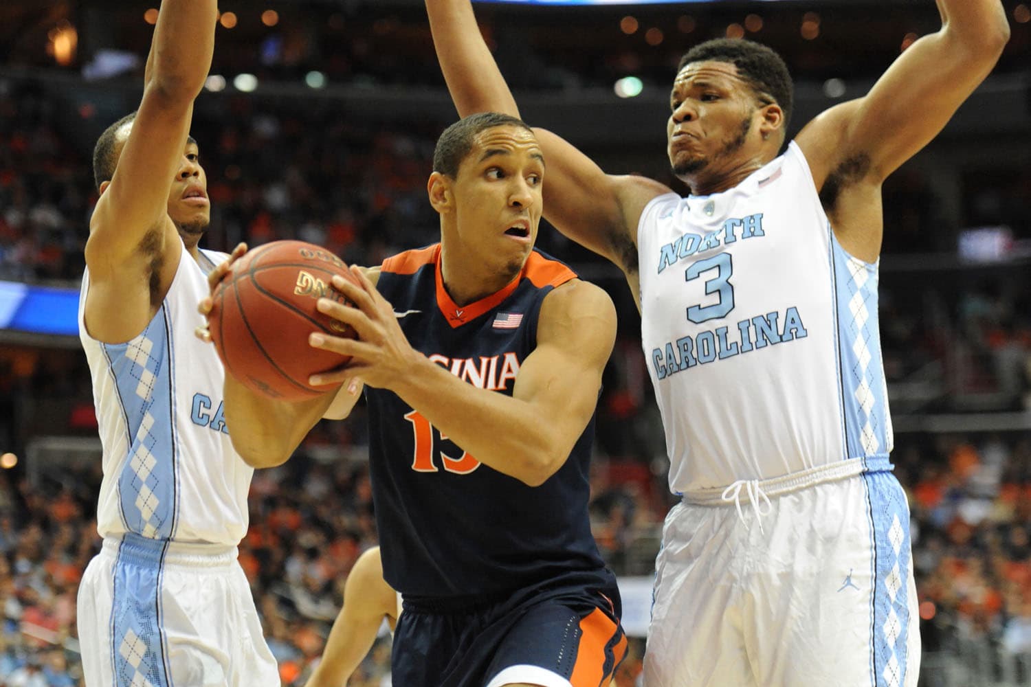 Malcolm Brogdon of the Virginia Cavaliers, wearing jersey number 15, dribbling the basketball down the court during a high-stakes game. His focused expression and athletic stance highlight his skill and determination. The crowd is visible in the background, adding to the intensity of the moment.
