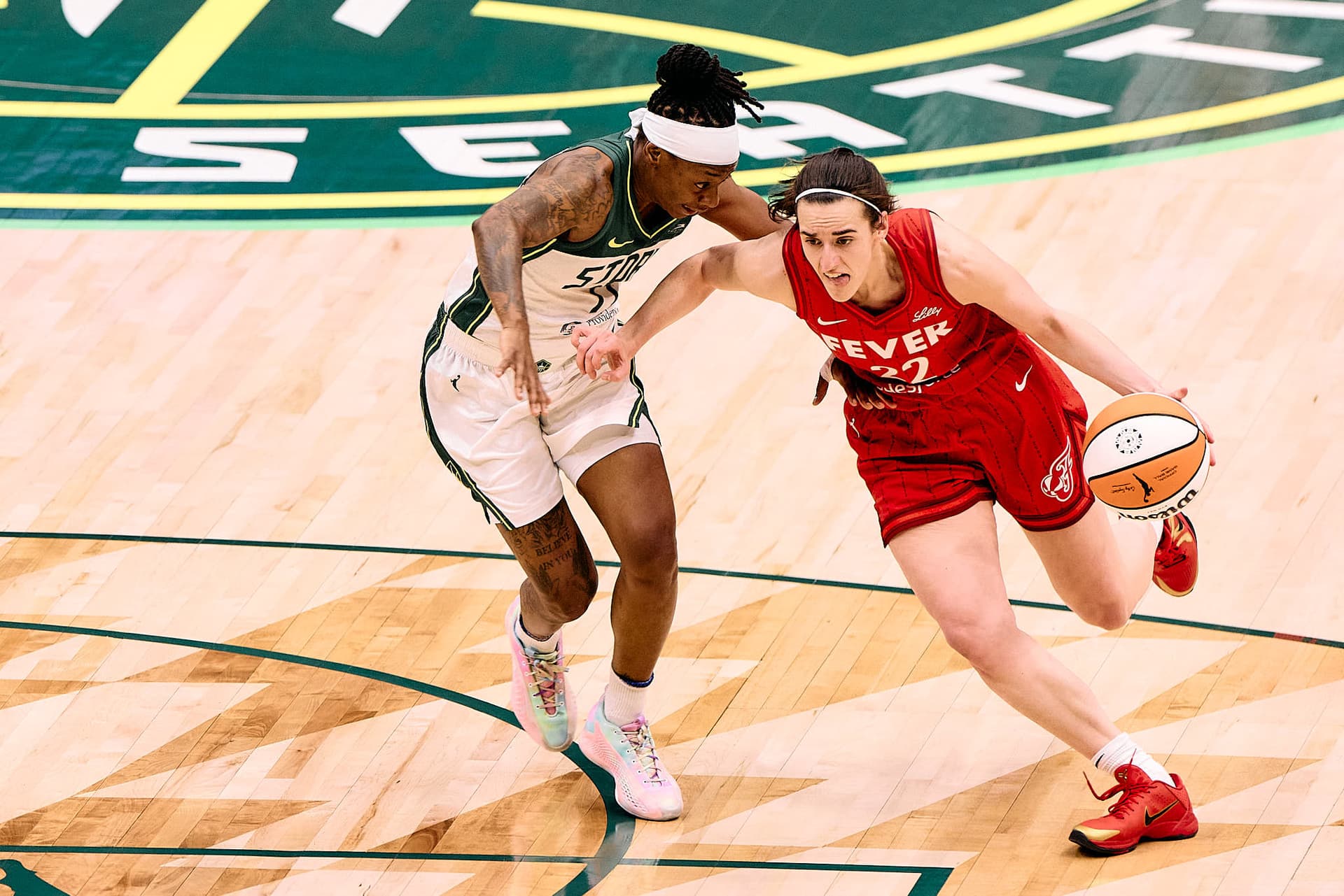 Caitlin Clark of the Indiana Fever dribbles up the court under defensive pressure from Erica Wheeler of the Seattle Storm during a WNBA basketball game at Climate Pledge Arena in Seattle, Washington, June 24, 2025. Action sports photography capturing elite women’s basketball athletes in high-intensity professional play.