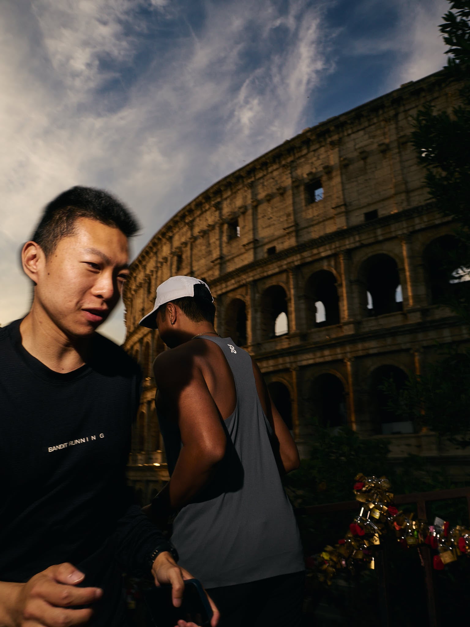 Two men in running gear stand in the foreground as the Colosseum rises behind them in warm evening light.